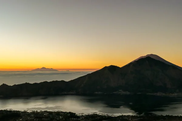 A morning golden hour seen from top of Mount Batur on Bali, Indonesia. There is Mount Rinjani in the back (Lombok) and Volcano Agung on the side. Fog in the valley. Mysterious and magical sunrise.