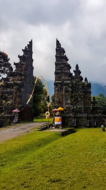 A view on the front of iconic Bali Handara Gate on a cloudy day. There are thick clouds around. The traditional Hindu gate to a gold course. Handara Gate is surrounded by lush green mountains