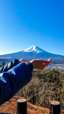 Holding Mt Fuji, Japan in both hands, on a clear, wintery day. The top parts of the volcano are covered with a layer of snow. There is an orange lantern on the side. Holly mountain of Japan.