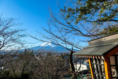 A distant view on Mt Fuji in Japan on a clear, wintery day. The top parts of the volcano are covered with a layer of snow. There is an orange lantern on the side. Holly mountain of Japan.
