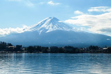 A close up view on Mt Fuji from the side of Kawaguchiko Lake, Japan. The mountain is hiding behind the clouds. Top of the volcano covered with a snow layer. Serenity and calmness. Calm lake's surface