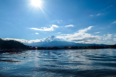 An idyllic view on Mt Fuji from the side of Kawaguchiko Lake, Japan. The mountain is surrounded by clouds. Serenity and calmness. The top of the volcano is covered with snow. Calm surface of the lake.