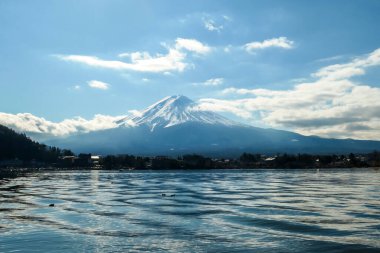 An idyllic view on Mt Fuji from the side of Kawaguchiko Lake, Japan. The mountain is surrounded by clouds. Serenity and calmness. The top of the volcano is covered with snow. Calm surface of the lake.