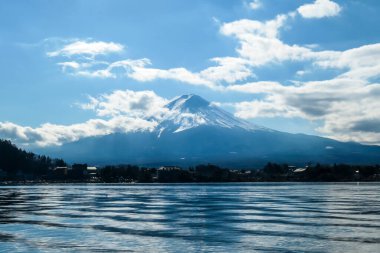 An idyllic view on Mt Fuji from the side of Kawaguchiko Lake, Japan. The mountain is surrounded by clouds. Serenity and calmness. The top of the volcano is covered with snow. Calm surface of the lake.