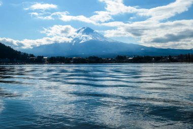 An idyllic view on Mt Fuji from the side of Kawaguchiko Lake, Japan. The mountain is surrounded by clouds. Serenity and calmness. The top of the volcano is covered with snow. Calm surface of the lake.
