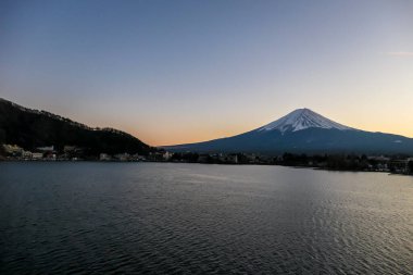 A view on Mt Fuji from the side of Kawaguchiko Lake, Japan. Soft colors of sunset - golden hour. Top of the volcano covered with a snow layer. Serenity and calmness. The lake's side is reed beds.