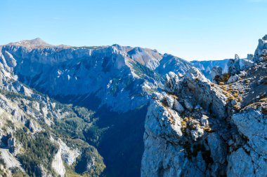 A man with a hiking backpack standing at the mountain ledge in Hochschwab region in Austria. There are many mountain ranges around her. The slopes overgrown with mountain pine, partially barren rocks