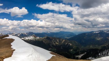 A panoramic view from top of Himmeleck in Austrian Alps. There is a massive mountain range in the back, partially covered with snow. Early spring vibes. barren mountain slopes. Overcast. Achievement