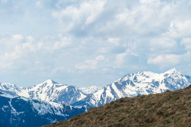 A distant view on the snowy slopes of Austrian Alps. There is a massive mountain chain in the back, partially covered with snow, barren meadow in the font. Early spring coming to the Alps. Overcast.