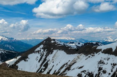 A distant view on the snowy slopes of Austrian Alps. There is a massive mountain chain in the back, partially covered with snow. Early spring coming to the Alps. Overcast. Achievement and fun.