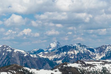 A distant view on the snowy slopes of Austrian Alps. There is a massive mountain chain in the back, partially covered with snow. Early spring coming to the Alps. Overcast. Achievement and fun.