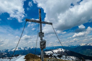 Wooden cross at the top of Himmeleck in Austrian Alps. There is a massive mountain range in the back, partially covered with snow. Early spring vibes. barren mountain slopes. Overcast. Achievement