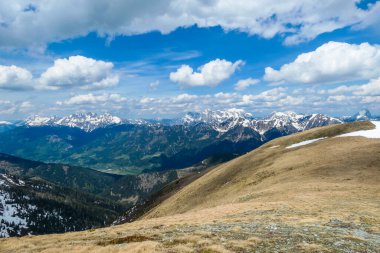 A vast view on Alpine valley from the upper parts of Himmeleck in Austria. The valley is lush green. There are many mountain ranges in the back, covered with snow. Spring coming to the Alps.