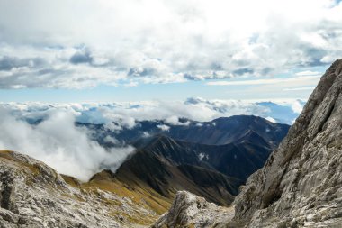 Sharp and rocky mountains range at Austrian-Italian border. There s a path mark on a stone. Serenity and peace. Clouds breaching high mountains. Lots of loose rocks, possibility of landslide