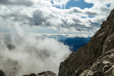 Sharp and rocky mountains range at Austrian-Italian border. There s a path mark on a stone. Serenity and peace. Clouds breaching high mountains. Lots of loose rocks, possibility of landslide