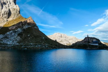 Panoramic shot of a soft reflection of an Alpine mountain in Wolayer Lake Austria. There is a mountain cottage at the shore. Mountain is catching the first sunbeams. Peace of mind, calmness.