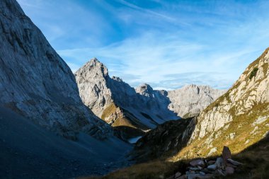 A pathway leading to high peaks in Italian Alps. Sharp slopes on both sides of the valley. Hard to reach mountain peaks. There are many mountain ranges in the back. Serenity and peace. Autumn vibes