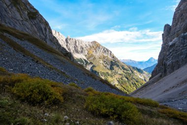 A close up shot of a massive mountain range in Austrian Alps. The rocky mountain looks inaccessible. High Alpine mountaineering. Sun rays coming from above the peaks. Lower parts are green