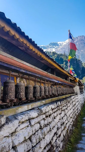 尼泊尔喜马拉雅山Annapurna环路旅行的石墙上布满了祈祷轮 墙上有一些祈祷旗 后面有一条高高的喜马拉雅山脉 — 图库照片