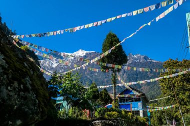 Colorful prayer flags waving above the Himalayan peaks along Annapurna Circuit Trek, Nepal. Meditation and peace of mind. High snow caped mountains peaks catching the first beams of sunlight