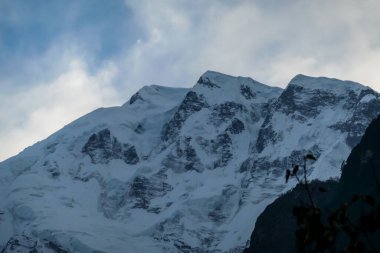View on Himalayan valley along Annapurna Circuit Trek, Nepal. There is a dense forest in front. High, snow caped mountains' peaks catching the sunbeams. Serenity and calmness. Barren slopes