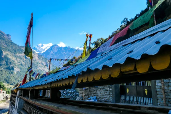 尼泊尔喜马拉雅山Annapurna环路旅行的石墙上布满了祈祷轮 墙上有一些祈祷旗 后面有一条高高的喜马拉雅山脉 — 图库照片