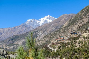 A Himalayan valley seen Annapurna Circuit Trek, Nepal. There is a small village on the side of the valley. In the back there are high snow caped mountains. Emptiness and serenity.