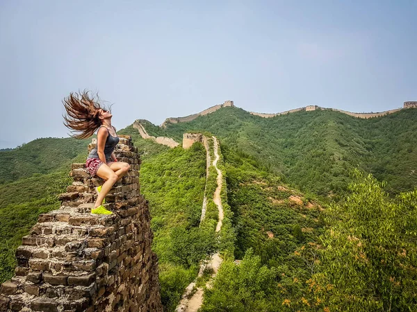 一个女人坐在中国的长城上 她让头发在风中飘扬 有了自由感和伟大的成就 攀登了世界奇迹之一 — 图库照片