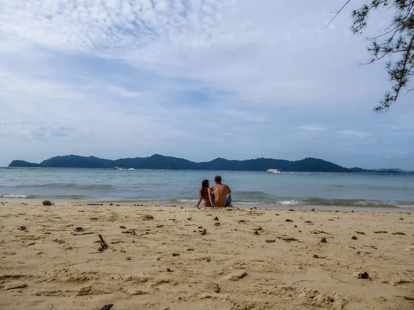 一对夫妇坐在沙滩边 他们穿着游泳衣 后部可见的其他岛屿 晴朗而好的天气 在岸边放松一下 一些侧边看得见的树枝 — 图库照片