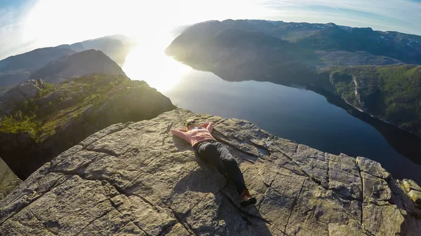 A girl lying at the edge of a steep cliff of Preikestolen, with a view on Lysefjorden. The girl enjoys the view, feeling free and happy. Steep fall dawn rising up the adrenaline level.