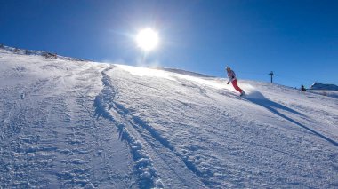 Snowboarder going down the slope in Goldeck, Austria. Perfectly groomed slopes. Crispy snow is thrown up under the pressure of the ski. A girl wears pink trousers, colorful jacket and protection helm