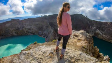 Woman standing at the volcano rim and watching the Kelimutu volcanic crater lakes in Moni, Flores, Indonesia. Woman is relaxed and calm, enjoying the view on lake shining with many shades of turquoise