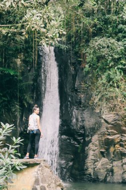 A girl is admiring the Murukeba waterfall in the small town of Moni, Island of Flores, Indonesia. The surrounding rainforest creates a magical atmosphere of inspiration and dedication.