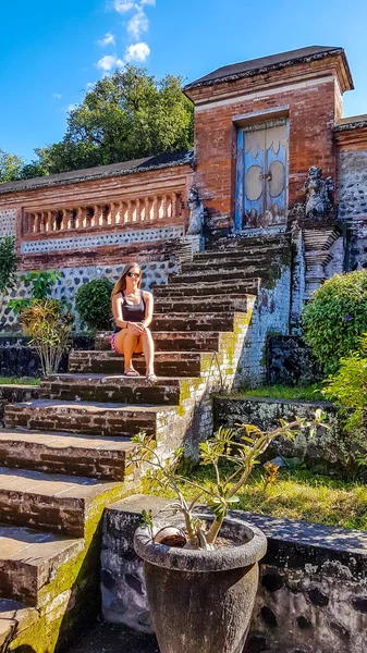 女孩坐在通往印度尼西亚伦博克一座寺庙的楼梯上 她正在享受她的时光和美丽的天气 旁边的花盆 发现新的地方 文化和传统 — 图库照片