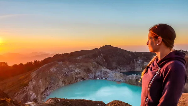 A woman watching the sunrise over the Kelimutu volcanic crater lakes in Moni, Flores, Indonesia. Woman is relaxed and calm, enjoying the view on turquoise lake. Golden hour over the volcano