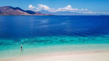 A drone shot of a girl playing on the beach on a small island near Maumere, Indonesia. Happy and careless moments. The coast changes colors from white to turquoise and navy blue. There are few islands