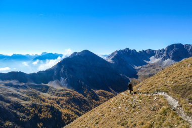 A woman with big hiking backpack walking on a pathway to reach the Grosse Gamswiesenspitze in Lienz Dolomites, Austria. Sharp slopes. Massive Alpine mountains. Solo wanderer, contemplating the nature