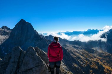 Woman in pink standing on the top of Grosse Gamswiesenspitze in Lienz Dolomites, Austria. Sharp, dangerous slopes. Massive Alpine mountains. Solo wanderer. She is happy and proud of her achievement