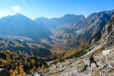 A woman with big hiking backpack walking on a pathway to reach the Grosse Gamswiesenspitze in Lienz Dolomites, Austria. Sharp slopes. Massive Alpine mountains. Solo wanderer, contemplating the nature