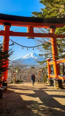 Woman standing under the Torri gate, leading to Chureito Pagoda in Japan and Mt Fuji in the back, on a clear, wintery day. The top parts of the volcano are covered with a layer of snow. Holly mountain