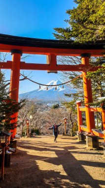 Woman standing under the Torri gate, leading to Chureito Pagoda in Japan and Mt Fuji in the back, on a clear, wintery day. The top parts of the volcano are covered with a layer of snow. Holly mountain