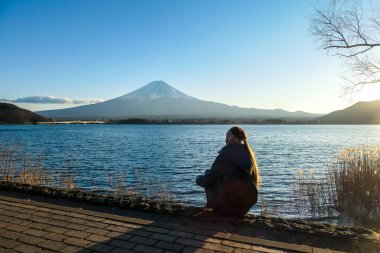 Kawaguchiko Gölü 'nün kenarında oturan ve Japonya' daki Fuji Dağı 'nı izleyen bir kadın. Dağ bulutlarla çevrili, tepesi karla kaplı. Yeni yerler keşfetmek. Huzur. Yumuşak günbatımı renkleri