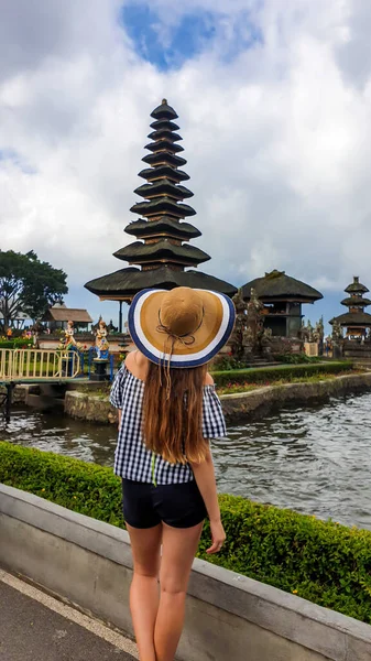 一名身穿短裤和草帽的妇女站在印度尼西亚巴厘岛乌鲁恩达努寺主楼前 这个女孩正在欣赏印度教水寺的美丽 神圣的地方发现新的文化 — 图库照片
