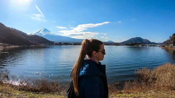 A woman standing at the side of Kawaguchiko Lake, Japan with the view on Mt Fuji. The magnificent mountain surrounded by clouds. Woman enjoying the beautiful landscape. Serenity and calmness