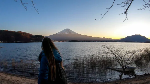 A girl walking at the side of Kawaguchiko Lake, Japan with the view on Mt Fuji. She is enjoying the moment, having a lot of fun. Soft colors of sunset. The volcano surrounded by clouds. Serenity