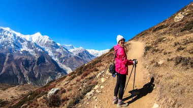 A woman trekking on the Annapurna Circuit Trek, Himalayas, Nepal. Panoramic view on snow caped Annapurna chain. Lots of dried grass. High altitude, massive mountains. Freedom and adventure