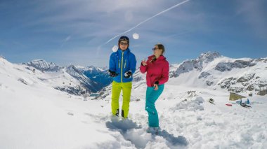 A couple in skiing outfits playing in the powder snow. They are throwing snow balls and laughing out loud, play time. Endless ranges of snow caped mountains in the back. Moelltaler Gletscher, Austria.