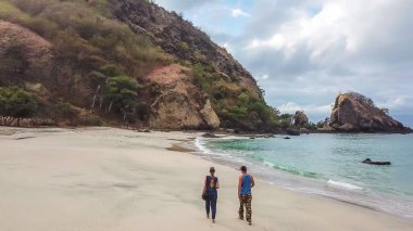 A couple walking on an idyllic Koka Beach. Hidden gem of Flores, Indonesia. Couple is enjoying their romantic escape. Waves gently washing the shore. There are hills in the back. Happiness and love