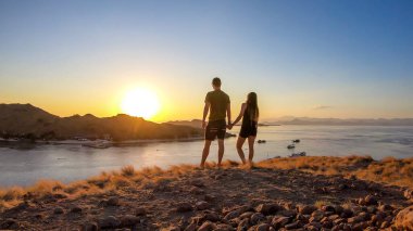 A couple walking on top of a small island, enjoying the morning sun over Komodo National Park, Flores, Indonesia. Golden hour over the islands and sea. They are enjoying their time. Love and happiness