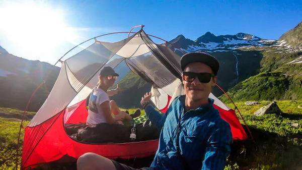 A couple camping in a wilderness. They sit in a small tent, placed on a top of a mountain peak, waiting for the sunset. High mountains around. Spring in alpine valleys. Happiness and togetherness.